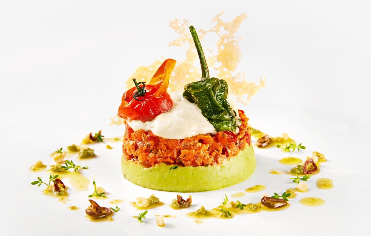 Die Vorspeise im PALAZZO Berlin: Tomaten-Oliven-Tatar auf cremiger Guacamole mit lauwarmem Parmesanschaum, Pimento und Basilikum-Vinaigrette