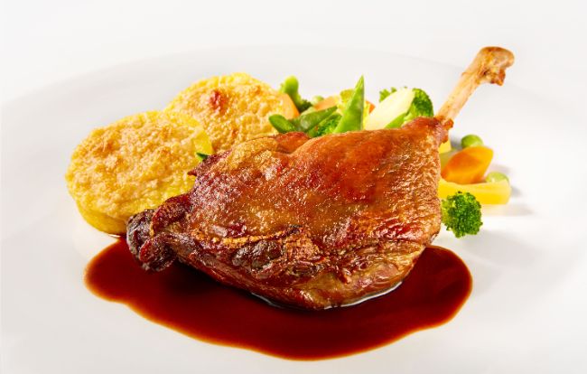 Der Hauptgang Confierte Entenkeule an Balsamico-Jus mit überbackenen Polentatalern und Wurzelgemüse im PALAZZO Berlin.