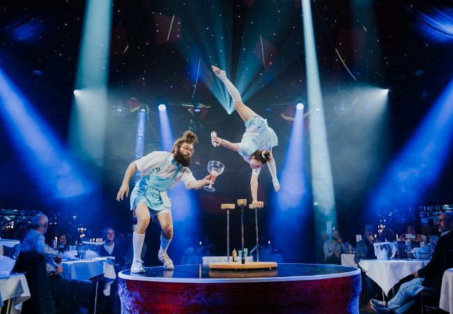 Die Künstlerin Danielle Saulnier macht einen Handstand während ihr Kollege komödiantisch umher läuft im PALAZZO.