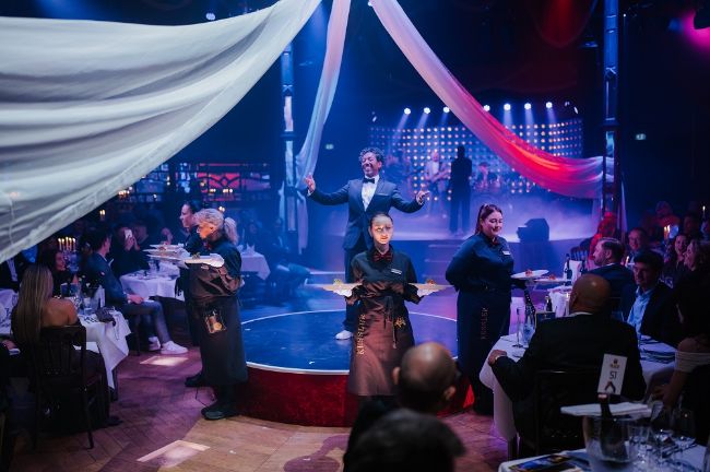 Daniel Reinsberg kündigt die Vorspeise an während die Servicekräfte um die Bühne des PALAZZO stehen.